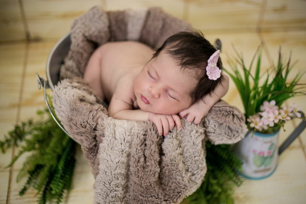 Baby im Eimer mit brauner Kuscheldecken und Schleife im dunklen Haar
