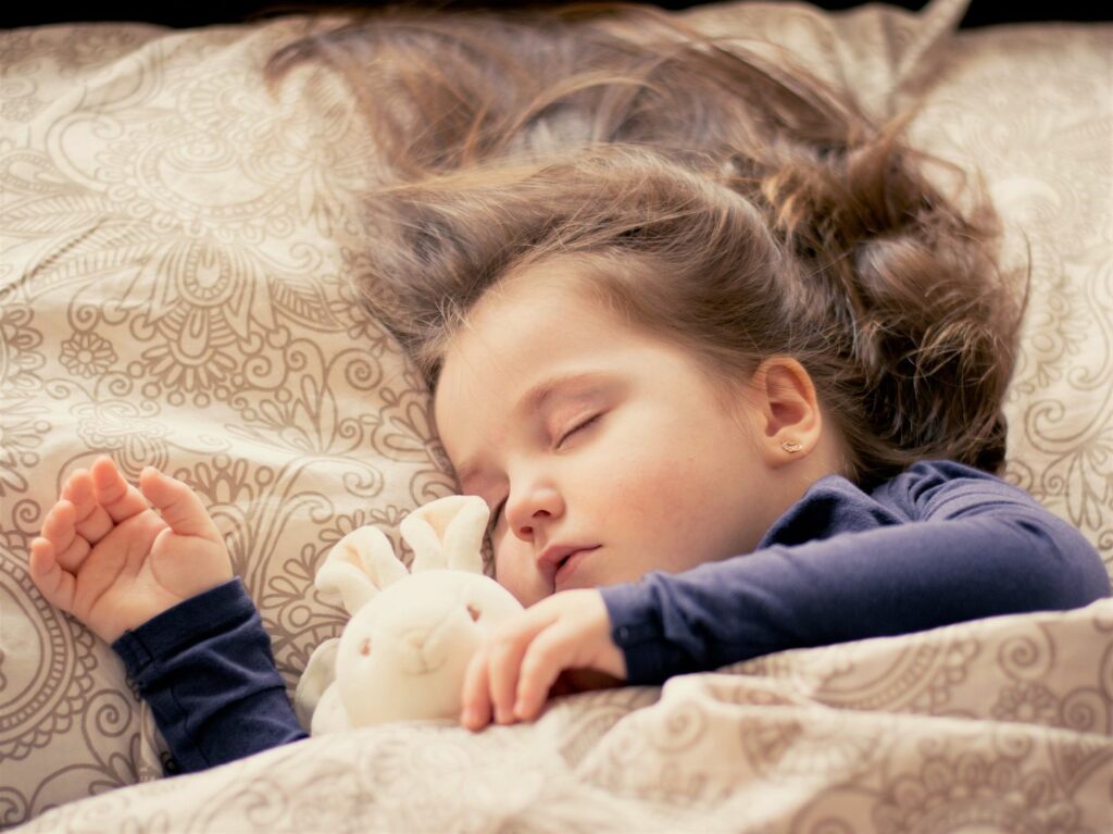 schlafendes, Kindergartenkind mit Plüschhäschen im Bett