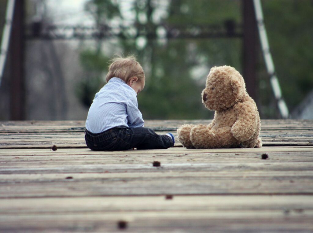 kleiner Junge sitz mit großem Plüschbar auf Holzbrücke