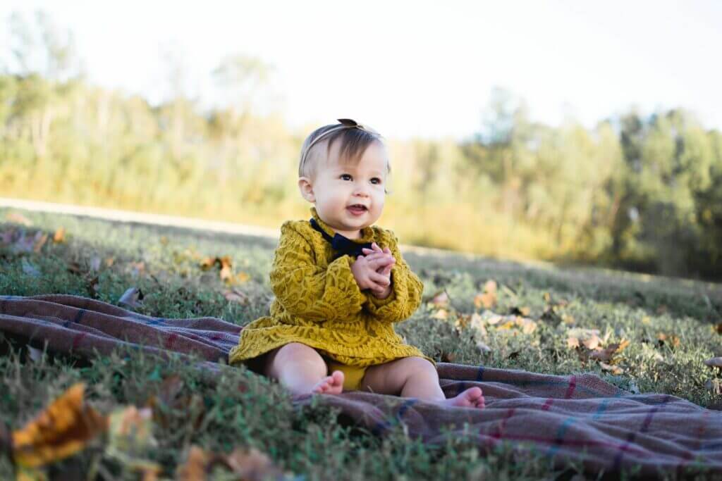 kleines Mädchen im gelben Kleid, sitzt auf der Decke auf einer Wiese