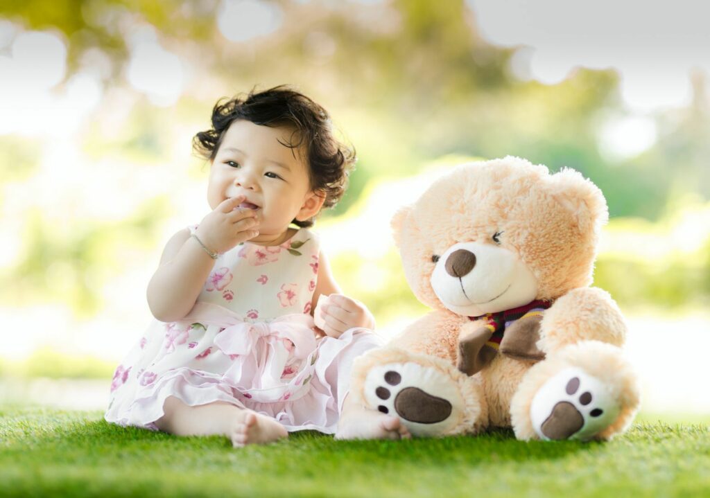 sitzendes kleines Mädchen in hübschem Sommerkleid mit riesigem hellem Plüschbären