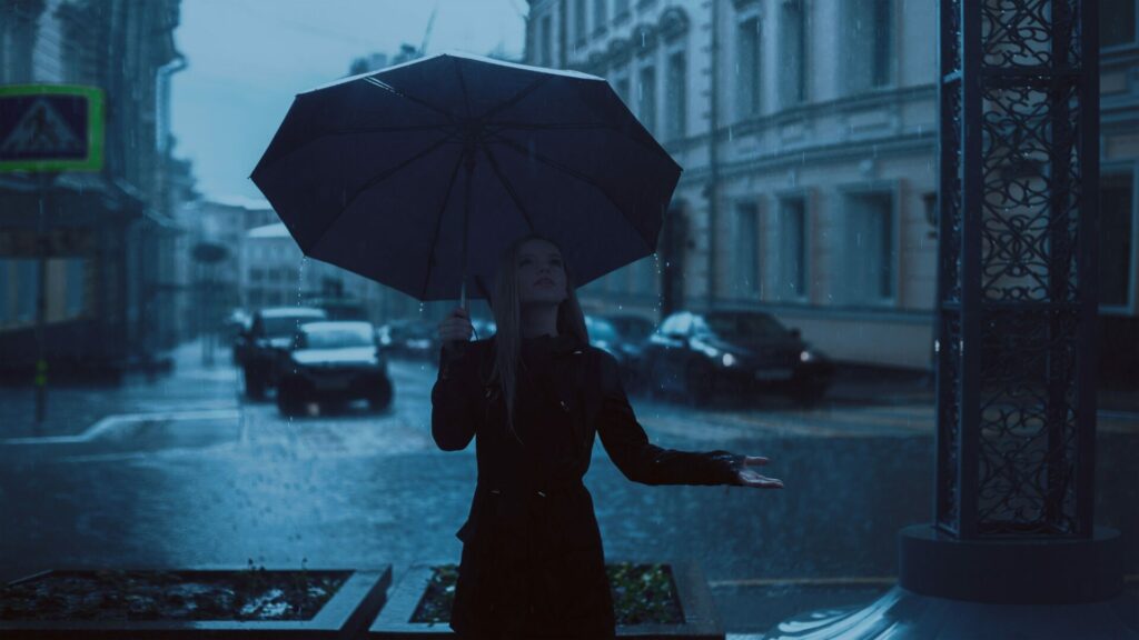 Frau mit großem Regenschirm hält die Hand raus um den Regen zu prüfen