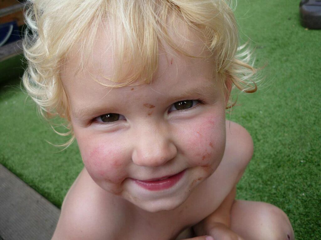 blondes Kleinkind mit schmutzigem Gesicht spielt im Garten