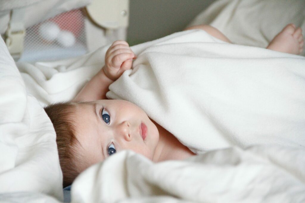 Baby mit großen blauen augen in weißer Bettwäsche