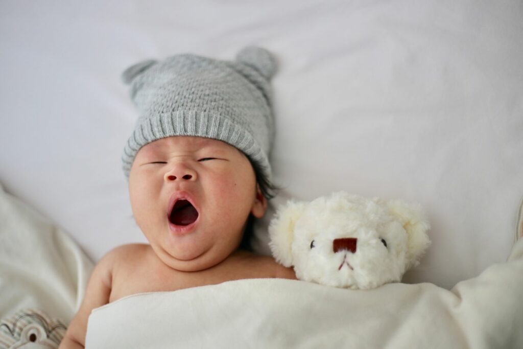 gähnendes Baby mit weißem Bärchen im Bett