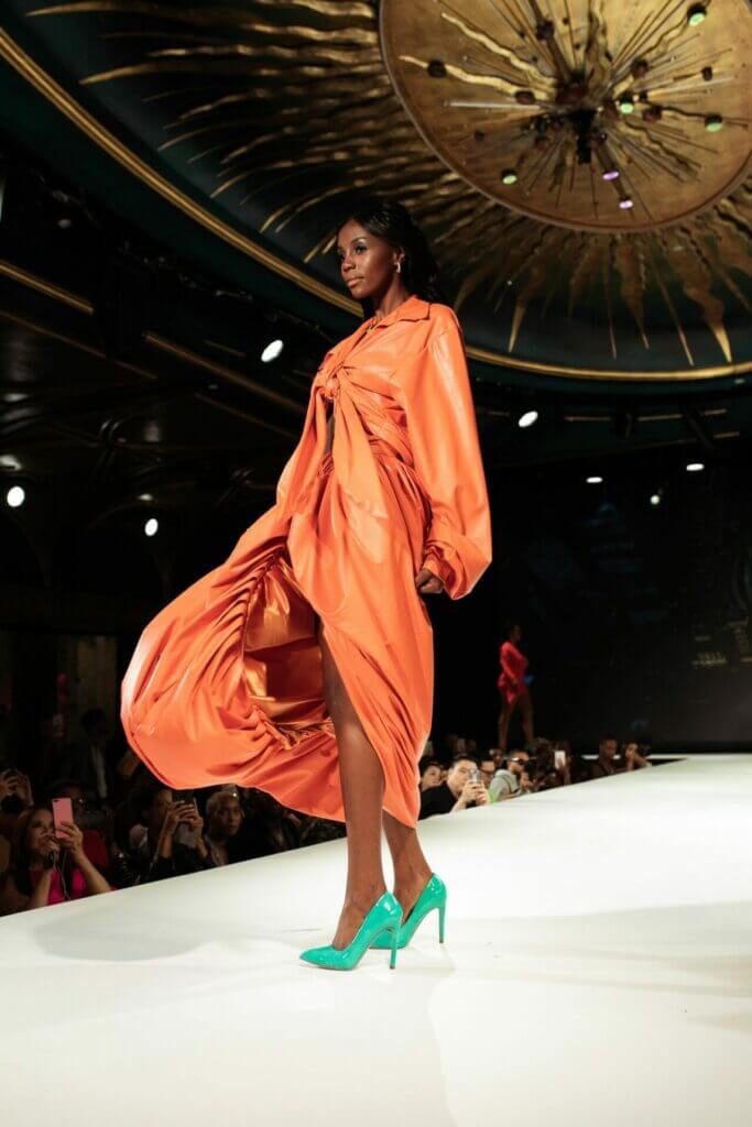 Frau im orangenen Designerkleid auf dem Laufsteg
